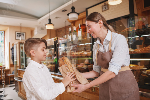 Friendly female baker giving freshly baked bread to her young customer