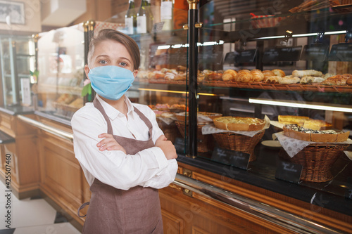 Young boy wearing medical face mask and apron, working at his family bakery shop, copy space