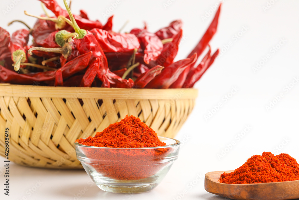 Dried red chilli and red chilli powder in glass bowl and wooden spoon on white background Dried red chilli and red chilli powder in glass bowl and wooden spoon on white background