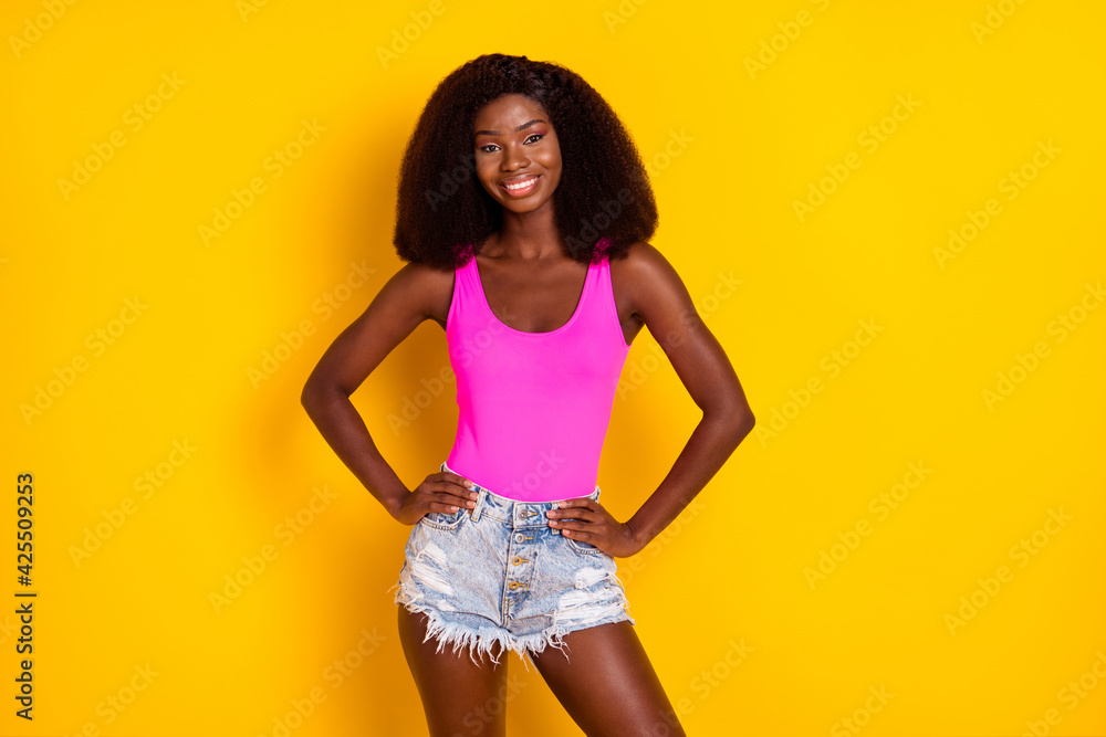 Photo of charming afro american girl put hands waist wear pink outfit isolated over shine yellow color background Photo of charming afro american girl put hands waist wear pink outfit isolated over shine yellow color background
