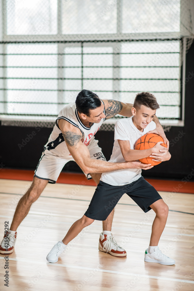 Dark-haired man playing basketball with a boy