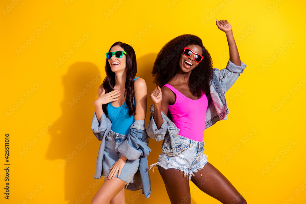 Photo of two crazy funny ladies carefree dance wear sunglass singlet jeans outfit isolated yellow color background Photo of two crazy funny ladies carefree dance wear sunglass singlet jeans outfit isolated yellow color background