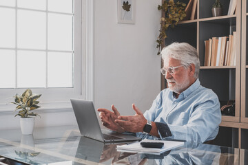 Happy old caucasian businessman smiling working online watching webinar podcast on laptop and learning education course conference calling make notes sit at work desk, elearning concept.
