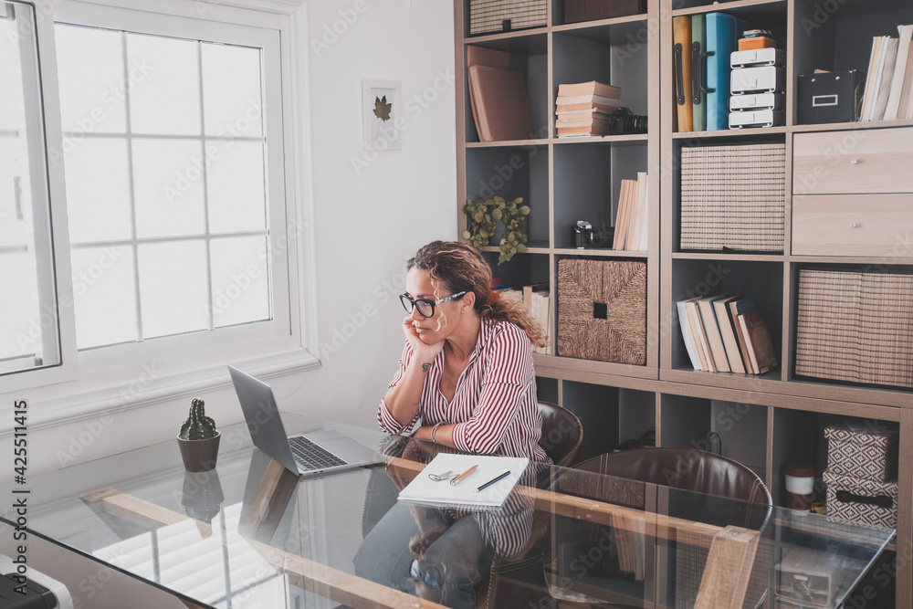 One young woman working at home in the office with laptop and notebook taking notes talking in a video conference. One businesswoman calling communicating. One young woman working at home in the office with laptop and notebook taking notes talking in a video conference. One businesswoman calling communicating.