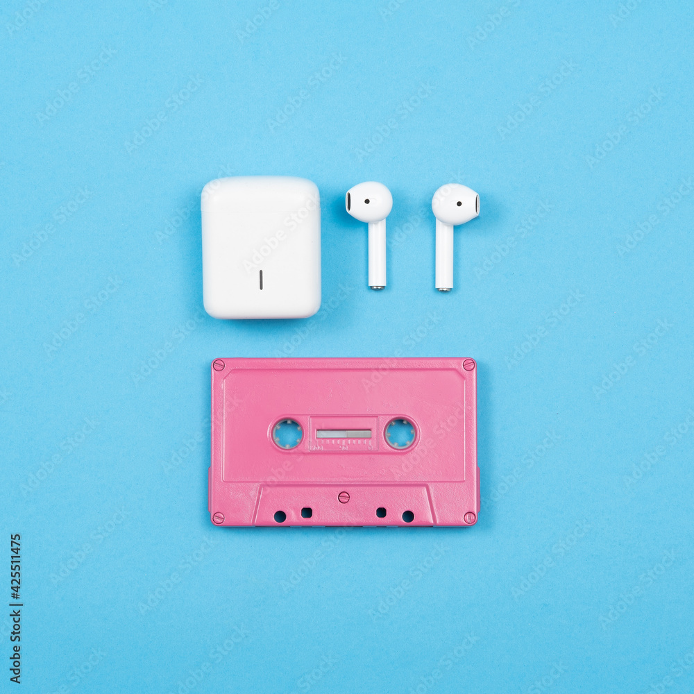 Fototapeta premium pink audio cassette with white wireless headphones on a blue background. stock photo
