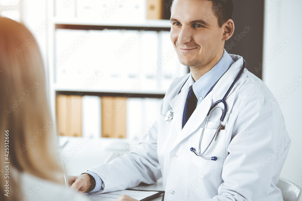 Friendly male doctor and patient woman discussing current health examination while sitting in clinic. Perfect medical service in hospital. Medicine and healthcare concept Friendly male doctor and patient woman discussing current health examination while sitting in clinic. Perfect medical service in hospital. Medicine and healthcare concept