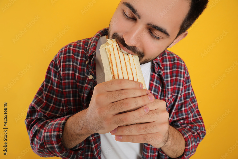 Young man eating tasty shawarma on yellow background, closeup Young man eating tasty shawarma on yellow background, closeup