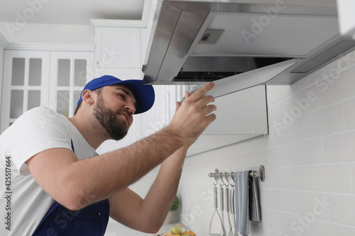 Worker repairing modern cooker hood in kitchen