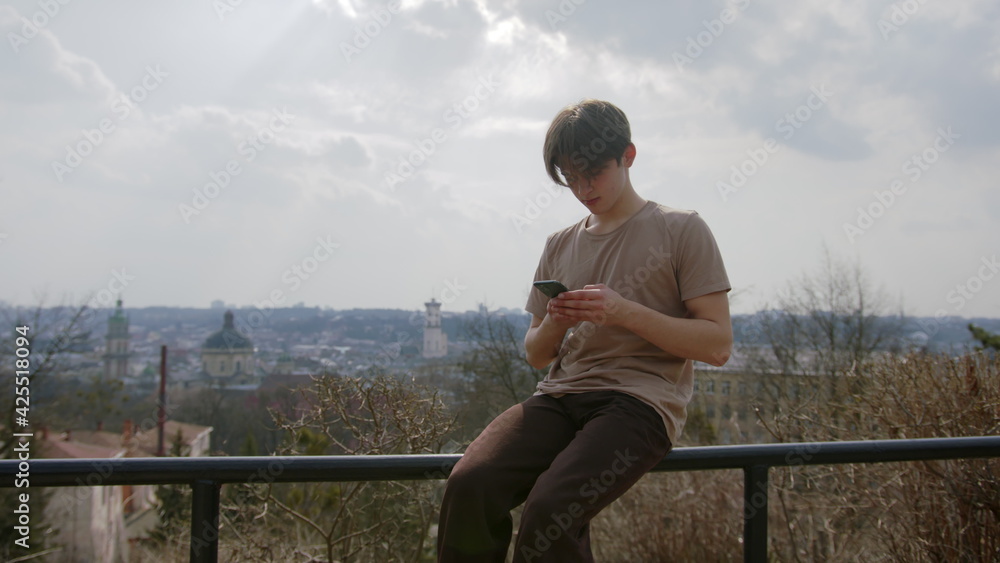 Young guy sitting on the railing and using a mobile phone Young guy sitting on the railing and using a mobile phone