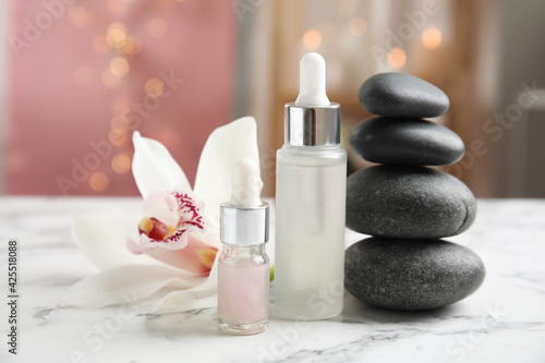 Essential oil, spa stones and orchid flower on white marble table against blurred lights