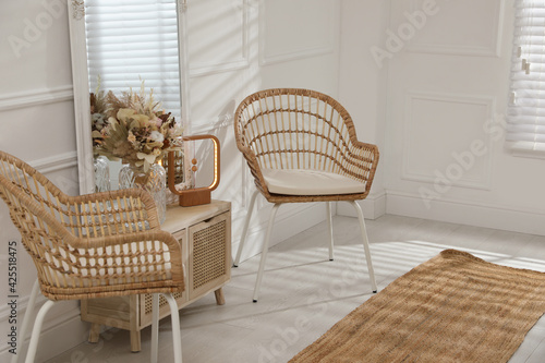 Living room interior with wooden commode, mirror and wicker chairs