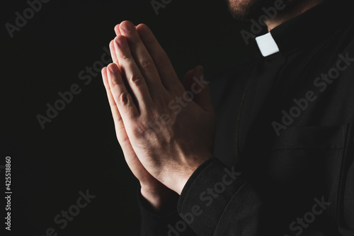 Priest in cassock praying on dark background, closeup