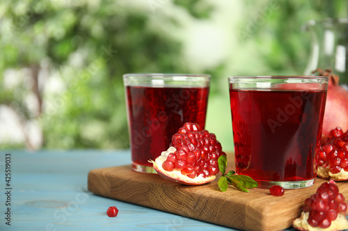 Pomegranate juice and fresh fruits on light blue wooden table outdoors  space for text