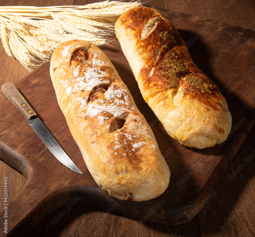 Breads, beautiful stuffed breads placed on wooden surface with branch of wheat, dark abstract background, selective focus.