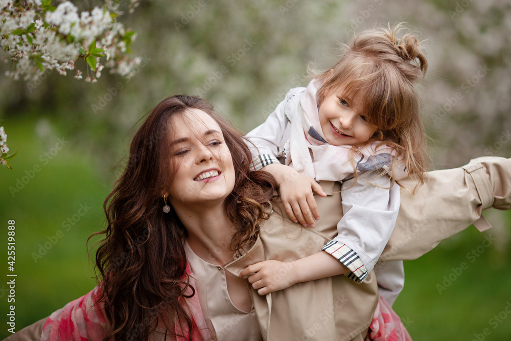 Mother with child girl playing in blooming spring garden. Woman with daughter huging and having fun outdoors. Concept of happy family