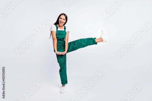 Photo of crazy party lady hold hands open mouth raise leg wear green overall sneakers isolated white color background photo