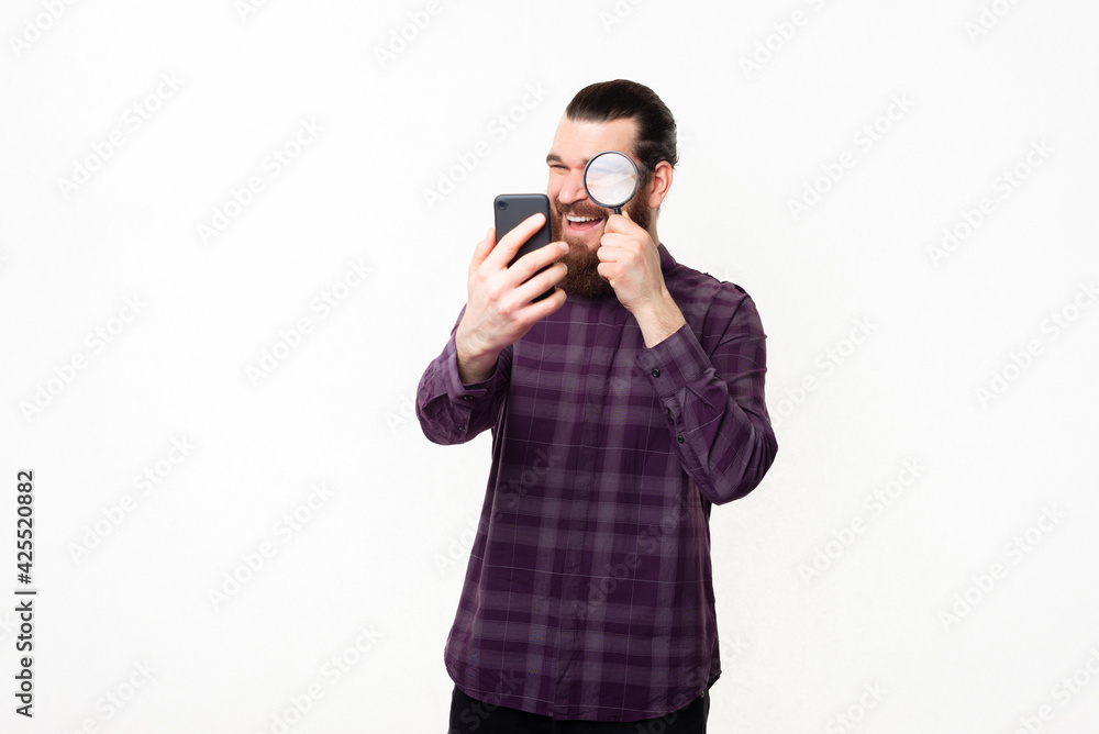 Photo of handsome man in checkered shirt looking trough magnifying glass at smartphone Photo of handsome man in checkered shirt looking trough magnifying glass at smartphone