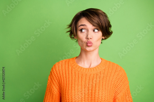 Portrait of optimistic brunette lady blow kiss look empty space wear orange sweater isolated on pastel green background