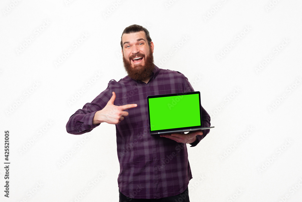 Photo of young man with beard in checkered shirt pointing at green screen on laptop Photo of young man with beard in checkered shirt pointing at green screen on laptop
