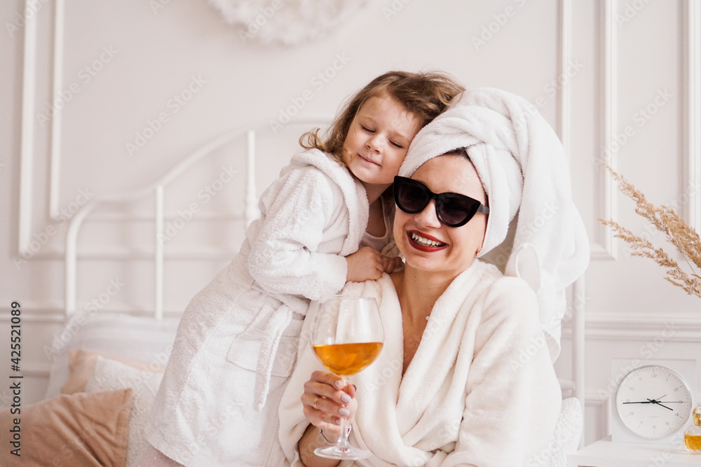 Mother and daughter in the bedroom in bathrobes. The girl hugs her mom