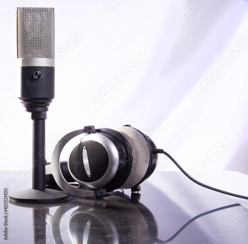 professional condenser microphone and headset on reflective surface and light background, selective focus.