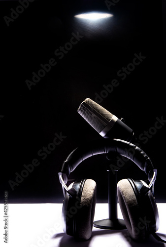 professional condenser microphone and headset on white surface and black background, low key portrait, selective focus.