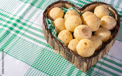 Cheese bread, heart-shaped basket lined with green and white fabric filled with cheese bread on a checkered tablecloth, selective focus.
