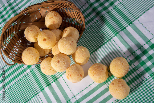 Cheese bread, fallen straw basket with cheese bread on a checkered tablecloth, top view. photo