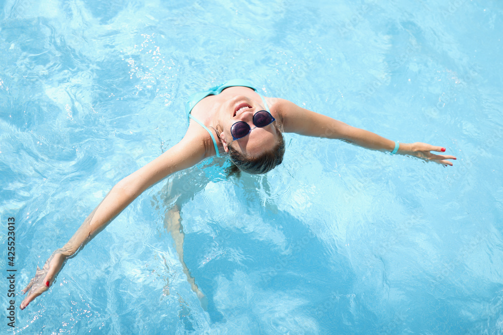 Young woman in sunglasses swimming in pool top view