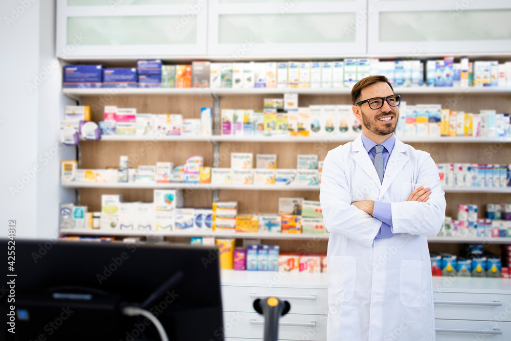Portrait of smiling caucasian pharmacist standing in drug store with arms crossed.