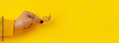 wooden snail in hand over yellow background, slowness concept, panoramic mock-up photo