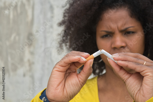 African american woman with afro hair and yellow t-shirt breaking a cigarette with her hands. photo