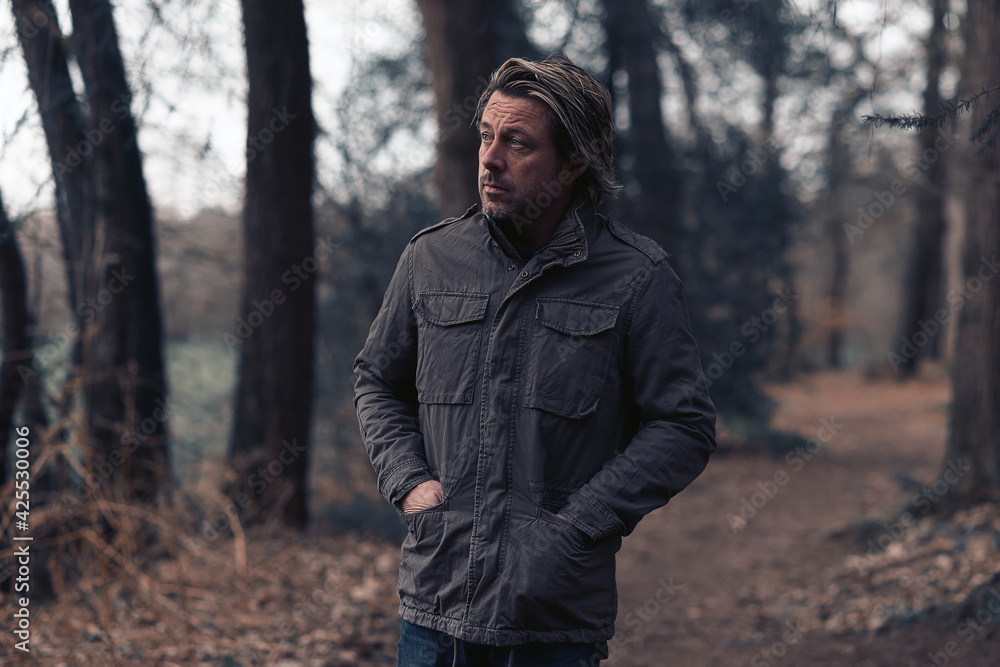 Blonde man in a green coat walks on a forest path. Blonde man in a green coat walks on a forest path.