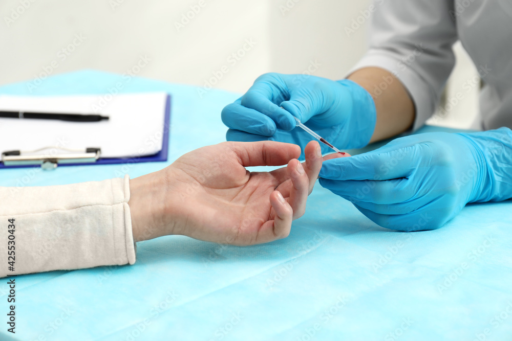 Doctor taking blood sample from patient's finger at table in clinic, closeup Doctor taking blood sample from patient's finger at table in clinic, closeup