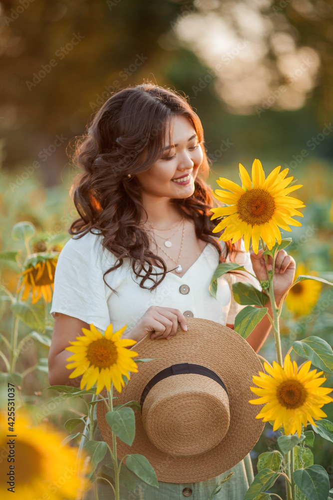 Young Asian woman with curly hair in a field of sunflowers at sunset. Portrait of a young beautiful asian woman in the sun. Young Asian woman with curly hair in a field of sunflowers at sunset. Portrait of a young beautiful asian woman in the sun.