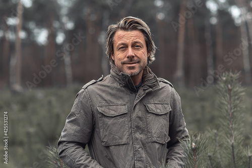 Smiling blond man in green coat in a field with young fir trees in a nature reserve. © ysbrandcosijn