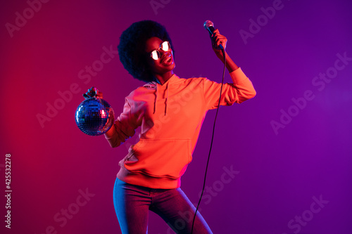 Photo of excited pretty lady hold microphone disco ball open mouth wear hoodie glasses isolated gradient neon background
