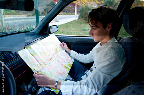 A Caucasian man from Spain sitting in his car and looking at a paper map - tourism and travel