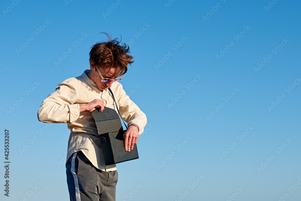 A Caucasian man from Spain standing and putting something in his black handbag on sky background A Caucasian man from Spain standing and putting something in his black handbag on sky background