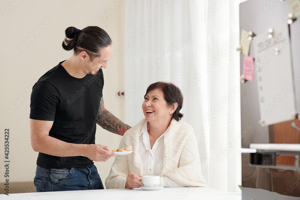 Cheerful caring adult son giving plate of homemade sugar cookies to mother visiting him at home Cheerful caring adult son giving plate of homemade sugar cookies to mother visiting him at home