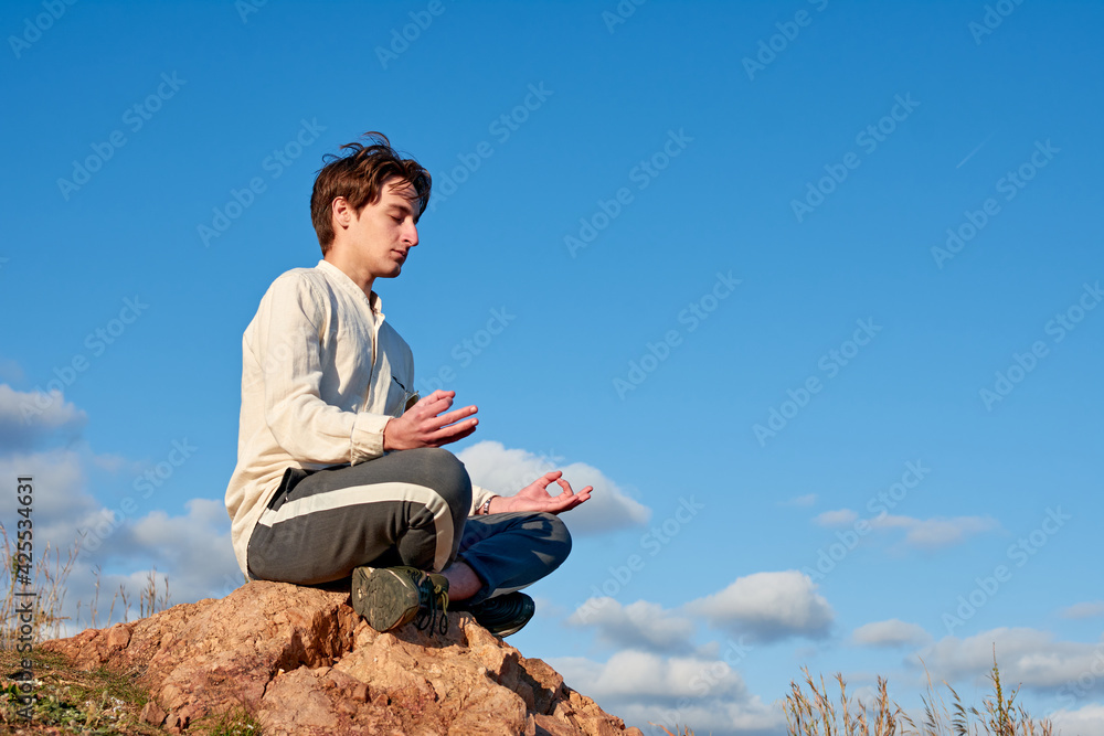 A Caucasian man from Spain sitting on a rock and meditating in grassy and disconnected area A Caucasian man from Spain sitting on a rock and meditating in grassy and disconnected area