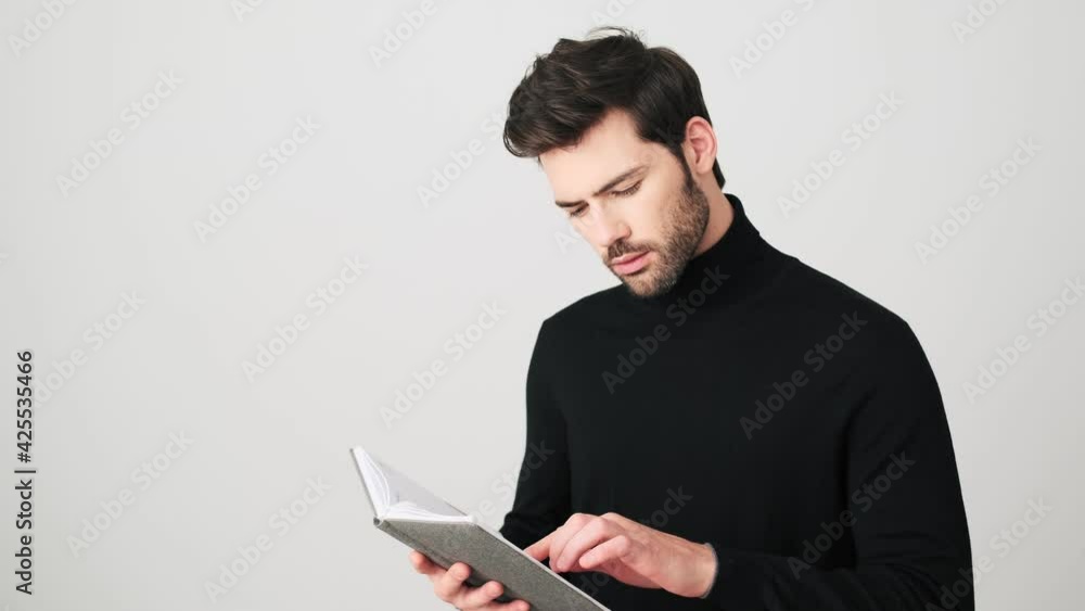 A handsome man is looking something in his copy-book standing over white background A handsome man is looking something in his copy-book standing over white background