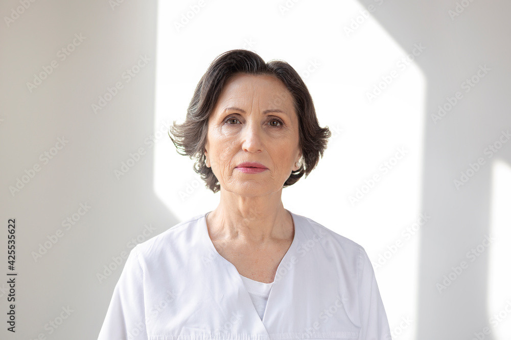 Portrait of serious adult female doctor in white medical coat on white background in the clinic Portrait of serious adult female doctor in white medical coat on white background in the clinic
