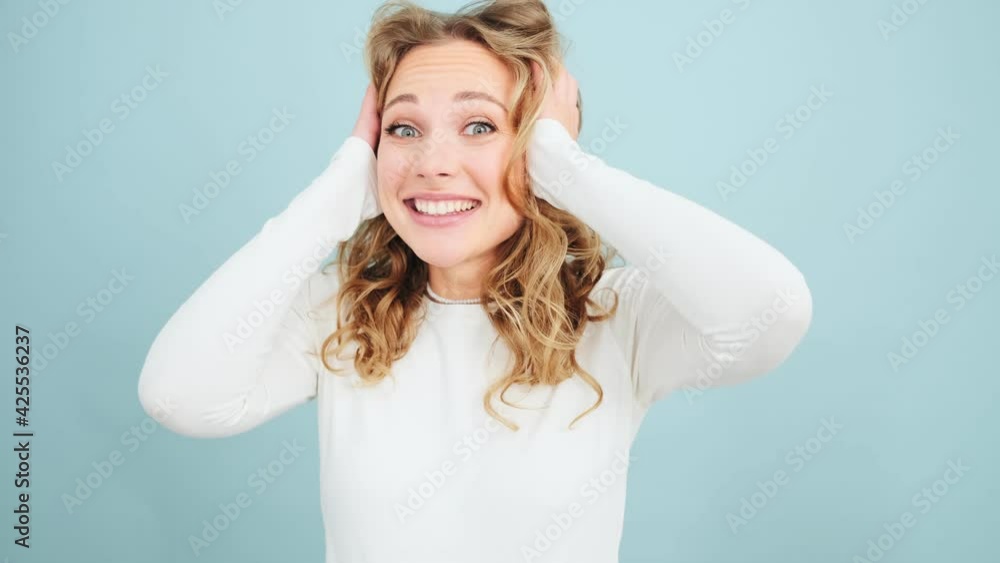 A surprised woman is looking to the camera standing isolated over blue wall in a studio A surprised woman is looking to the camera standing isolated over blue wall in a studio