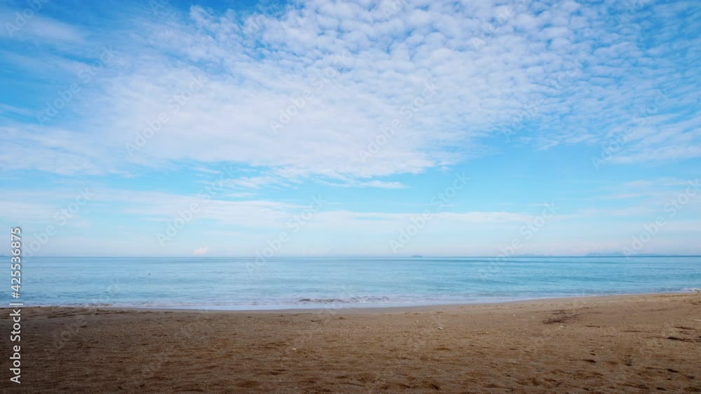 Empty and calm tropical beach at morning hours, light cirrus clouds on blue sky. Small waves softly wash sandy shore, nobody around. Horizon line seen in light mist Empty and calm tropical beach at morning hours, light cirrus clouds on blue sky. Small waves softly wash sandy shore, nobody around. Horizon line seen in light mist