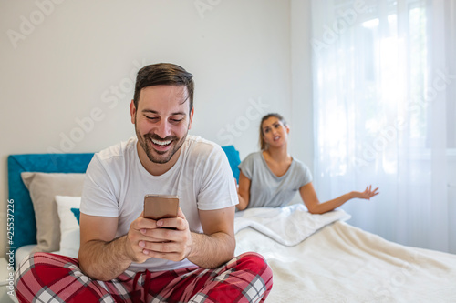 Woman looking unhappy while her man paying no attention to her and busy using his mobile phone. Sulking woman sitting next to man reading text messages during a morning.