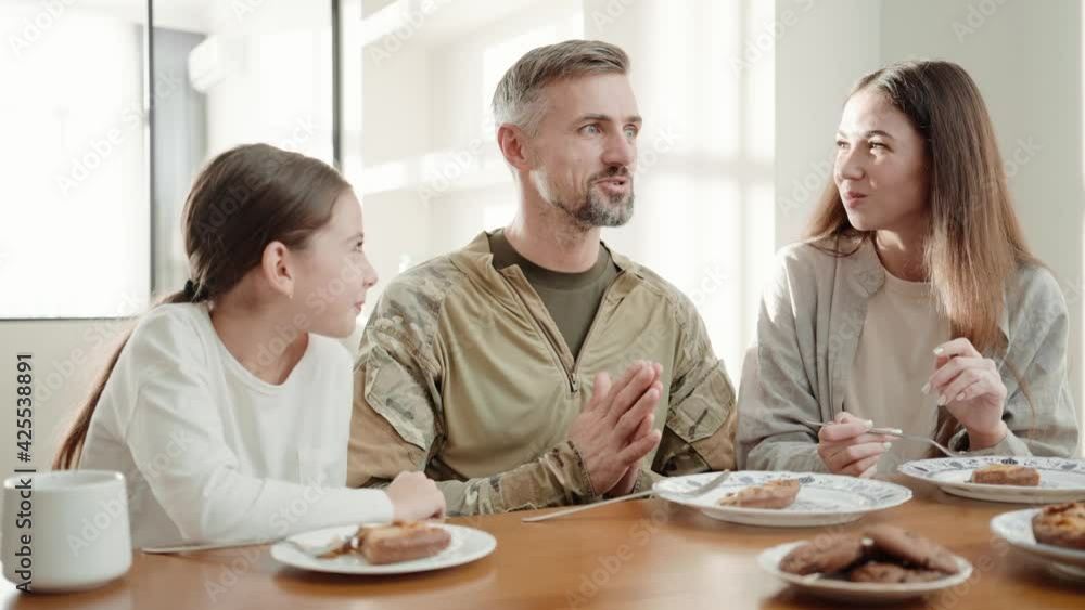 A positive soldier man is talking to this family while eating breakfast after returning from military service sitting in the white kitchen at home A positive soldier man is talking to this family while eating breakfast after returning from military service sitting in the white kitchen at home