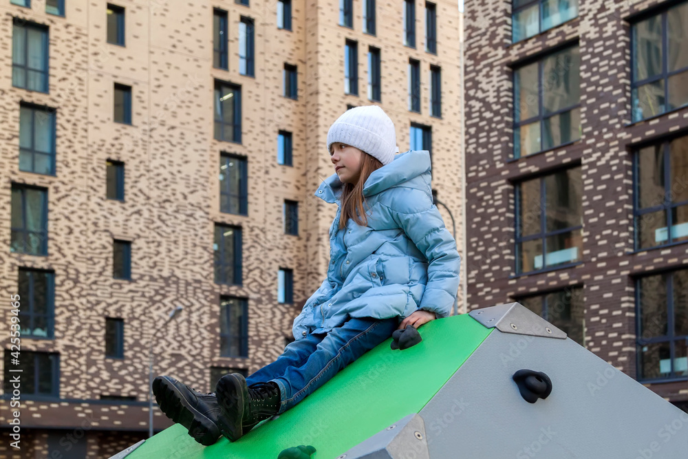 little girl on sunny spring day Smiling and having good time on kids climbing equipment on playground tightly squeezed residential buildings. Portrait of adorable child outdoors on spring day