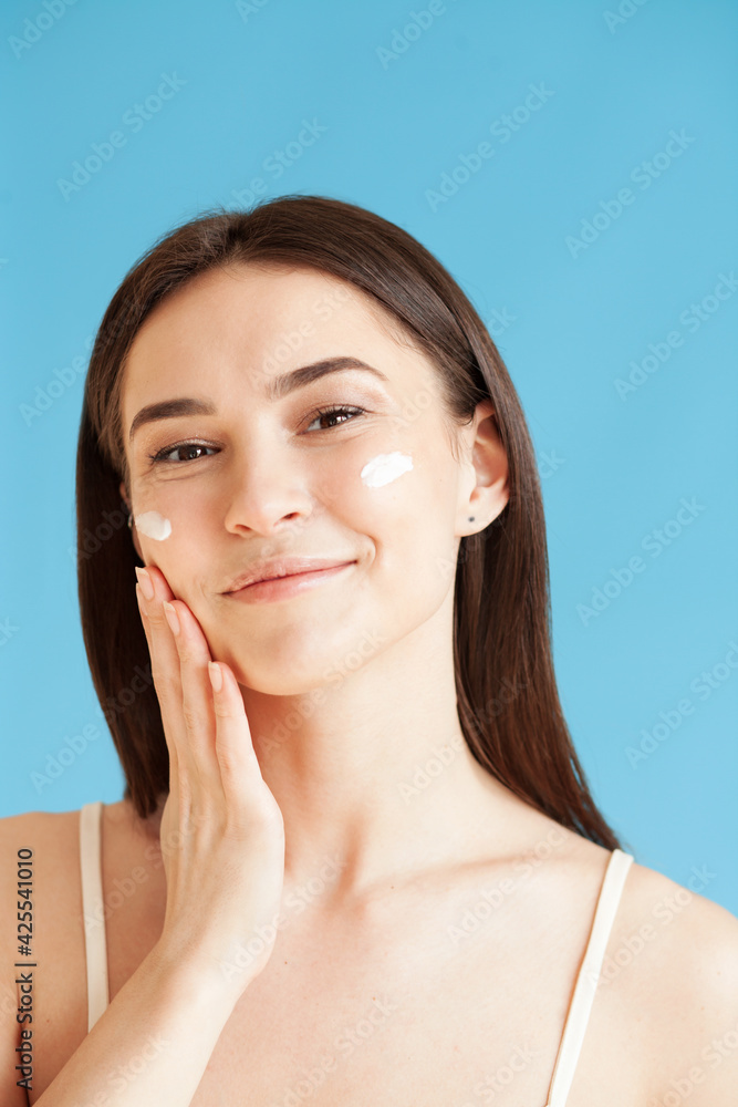 Lovely young woman with healthy skin is applying a cream on her face Lovely young woman with healthy skin is applying a cream on her face