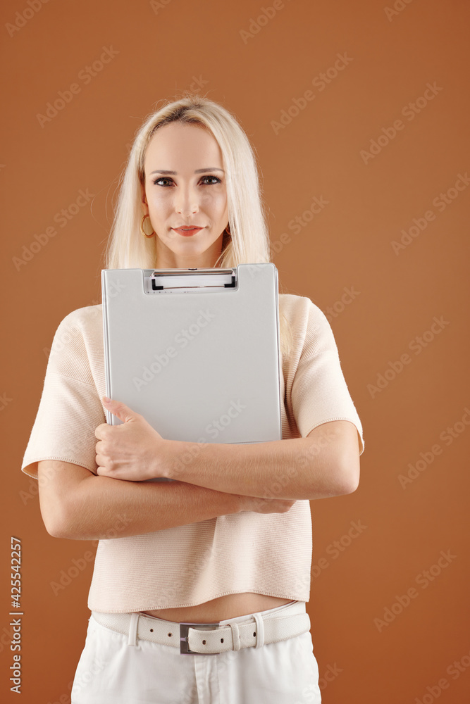 Young pretty female entrepreneur with clipboard posing agaiinst brown background and looking at camera Young pretty female entrepreneur with clipboard posing agaiinst brown background and looking at camera